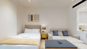 A modern hotel room with a bed, a sofa, a small table, and a nightstand. - Studio in JVC near Circle Mall l Pool & Gym (Jumeirah Village Circle)