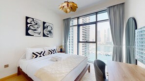 A hotel room with a bed, a desk, and a view of a marina through large windows. - Lux 1 Bed Partial Sea View l Private Beach Access (Emaar Beachfront)