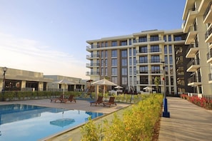 A modern hotel with a swimming pool, outdoor seating, and a multi-story building.