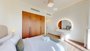 A hotel room with a bed, a wardrobe, a vanity with a mirror, and a small stool.