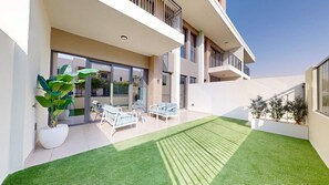 A modern outdoor patio with a lawn, seating area, and potted plants.