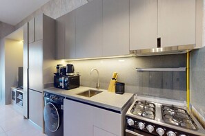A modern kitchen with a built-in washing machine, a coffee maker, and a gas stove. - Upgraded Studio in Meydan l Peaceful Community (Meydan)