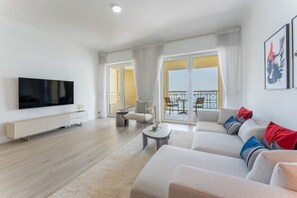 A modern living room with a flat-screen TV, a sofa set, a coffee table, and a balcony with outdoor furniture. - Spacious 2 Bed with Sea View in The Palm (Palm Jumeirah)