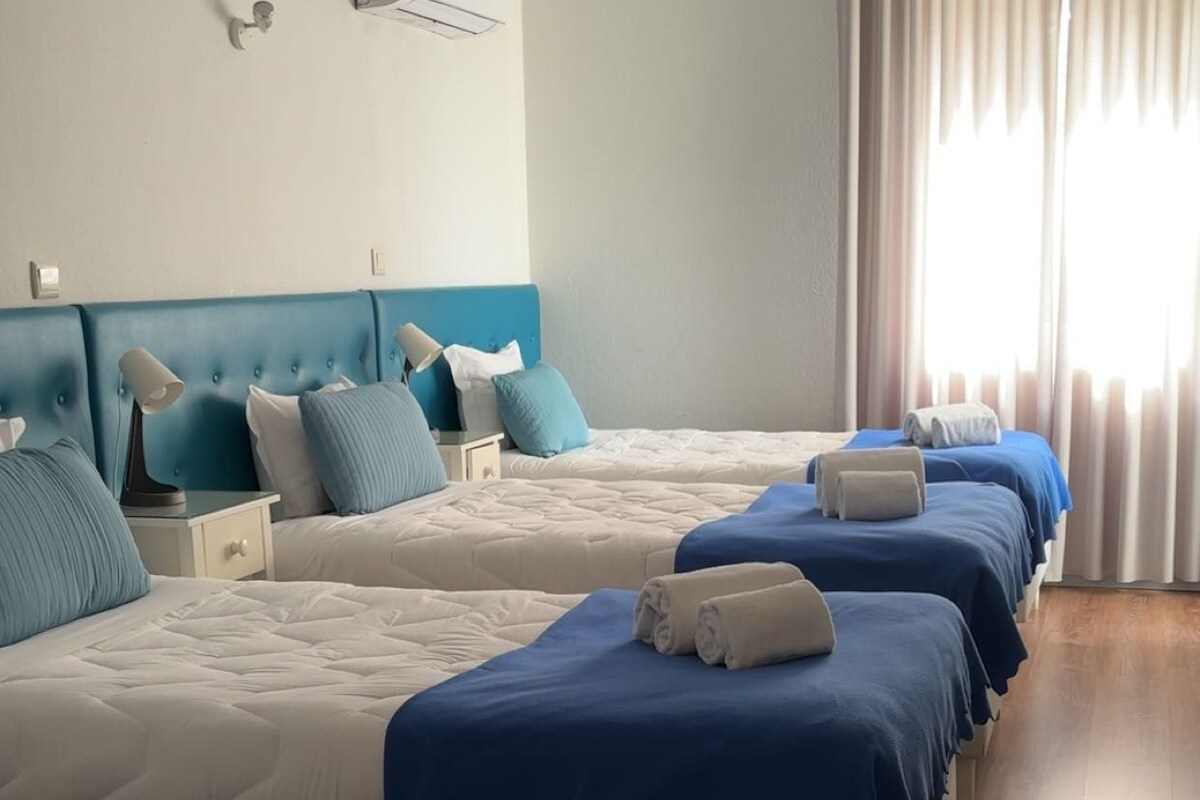 Une chambre d’hôtel avec plusieurs lits alignés, chacun étant recouvert d’une couverture bleue et agrémenté d’oreillers blancs.