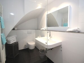 A modern bathroom with a white sink, a toilet, and a glass shower enclosure. - Island Love OG W3 (Sylt)
