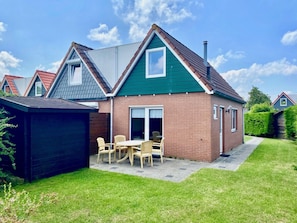 A residential house with a brick exterior, a green roof, and a patio with outdoor furniture. - Holiday Home With 2 Bedrooms (Oostkapelle)