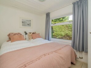 A bedroom with a bed, a bedside lamp, a framed picture on the wall, and a window with curtains. - Holiday Home in Renesse With Swimming Pool (Renesse)