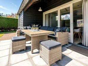 An outdoor patio with wicker furniture, a table, and a view of the interior through glass doors. - Holiday Home in Renesse With Swimming Pool (Renesse)