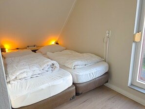 A bedroom with two beds, a window, and a wall-mounted light fixture. - Vr03 Holiday Home Breezand With dog (Vrouwenpolder)