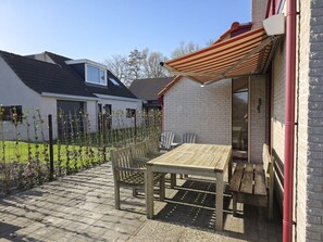 A patio with a table and chairs, a striped awning, and a brick wall. - Vr03 Holiday Home Breezand With dog (Vrouwenpolder)