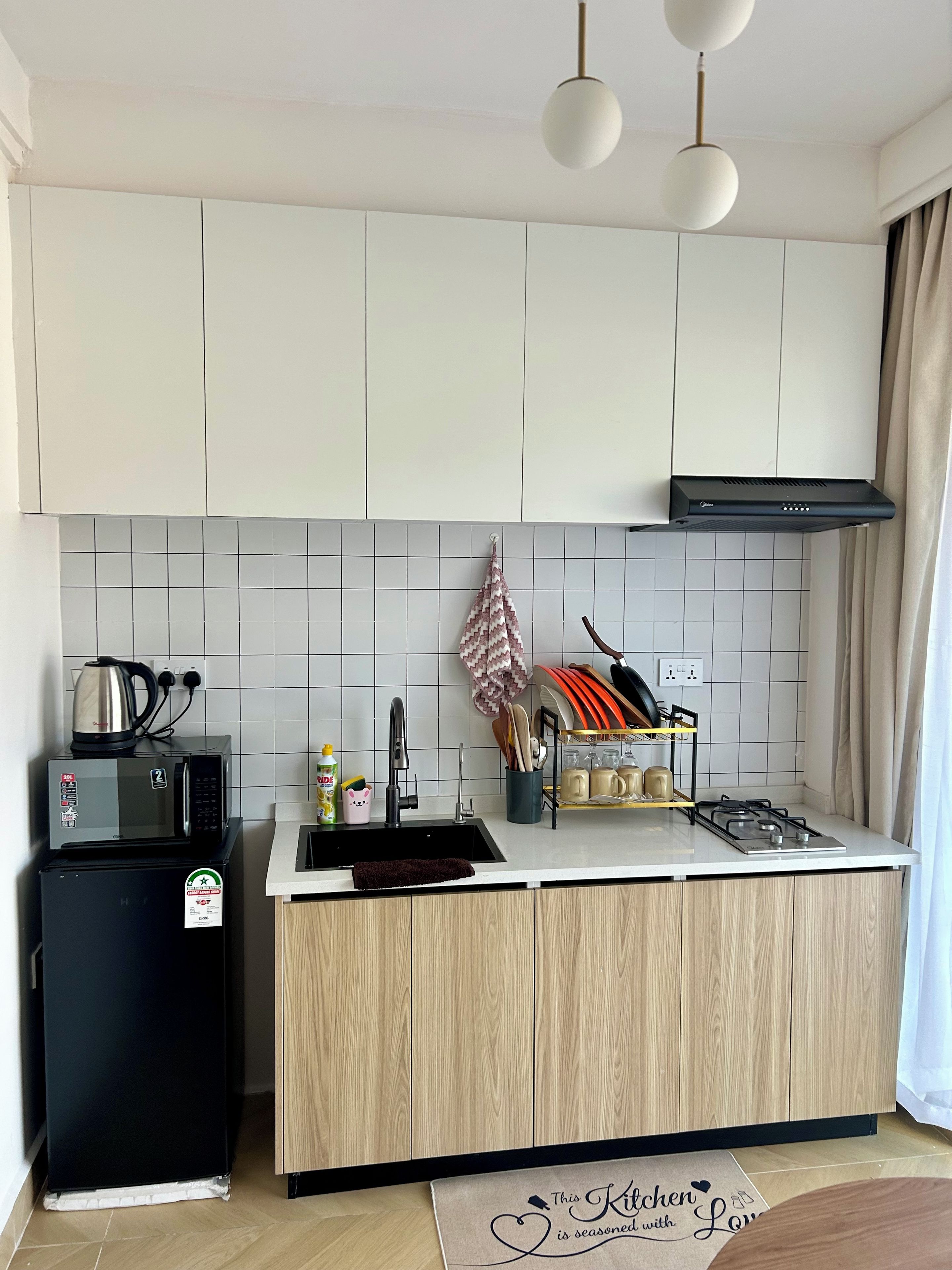 A modern kitchen with white cabinets, a black refrigerator, a microwave, a gas stove, and a hanging pot rack.