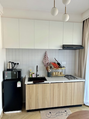 A modern kitchen with white cabinets, a black refrigerator, a microwave, a gas stove, and a hanging pot rack.
