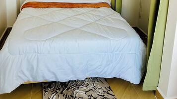 A neatly made bed with a headboard, a wall-mounted artwork, and a green curtain partially covering a closet.