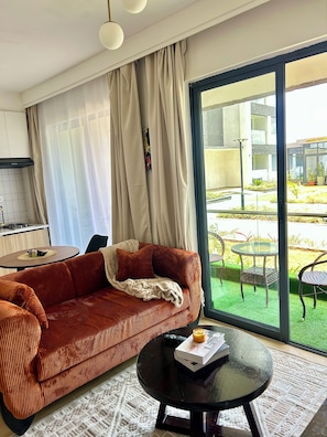 A modern living room with a sofa, a coffee table, and a view of an outdoor garden through a large window.
