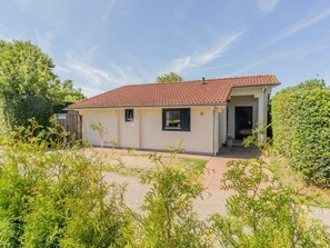 Ein eingeschossiges Gebäude mit einem Ziegeldach, einer kleinen Veranda und einem Garten im Vordergrund.