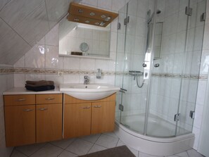 A bathroom with a glass-enclosed shower, a sink, and wooden cabinets. - Holiday Apartment With 2 Bedrooms (St. Peter-Ording)