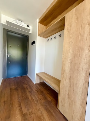 Ein Korridor mit Holzboden, einer dunklen Tür und einer weißen Wand mit Kleiderhaken.