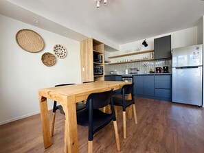 Eine moderne Küche mit Esstisch und Stühlen aus Holz, integrierten Regalen und einem Edelstahlkühlschrank.