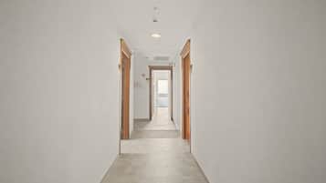 A long, narrow hallway with wooden doors on both sides, leading to a bright room at the end.