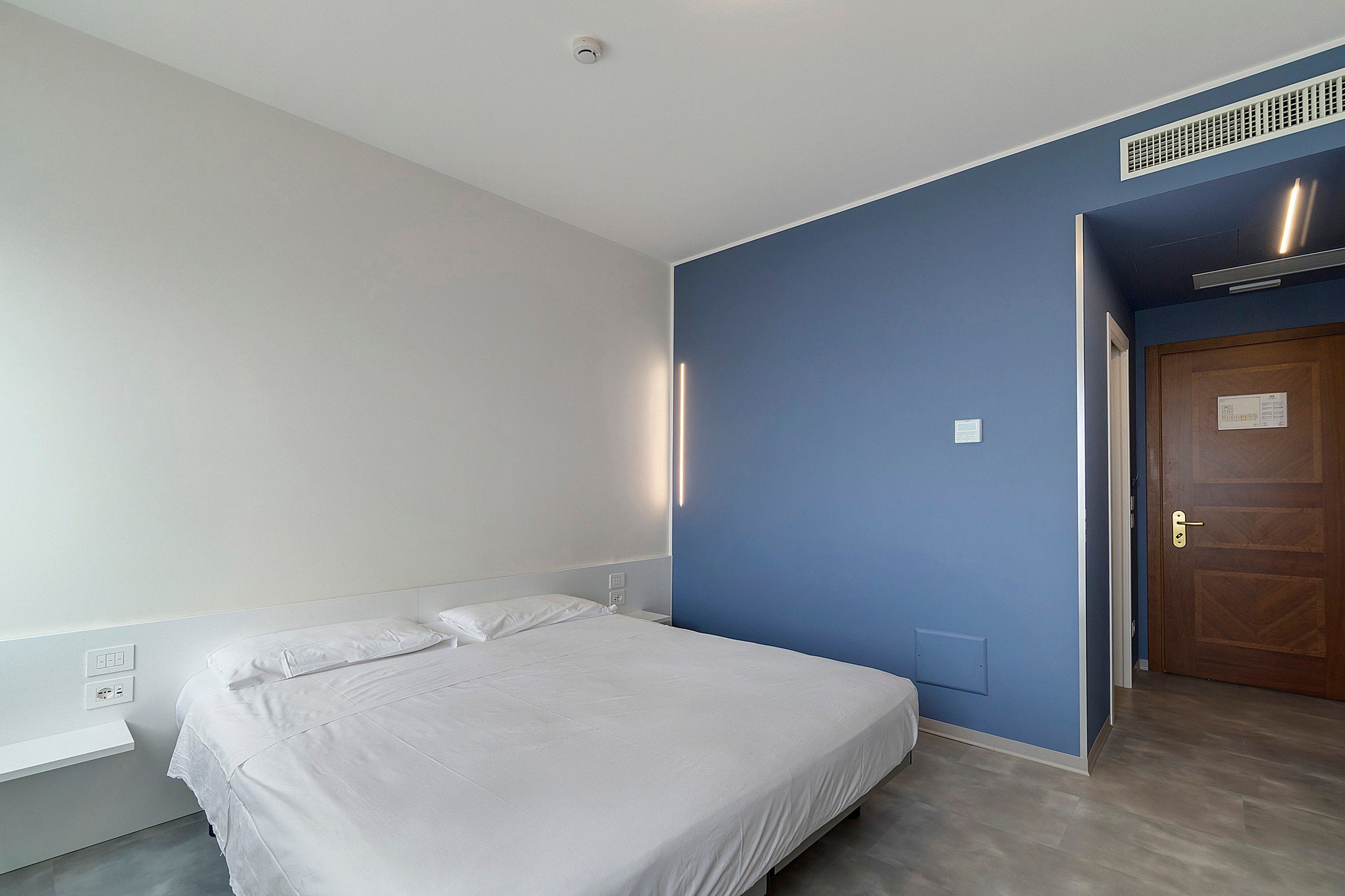 A bedroom with a single bed, a door, and a wall-mounted light fixture.