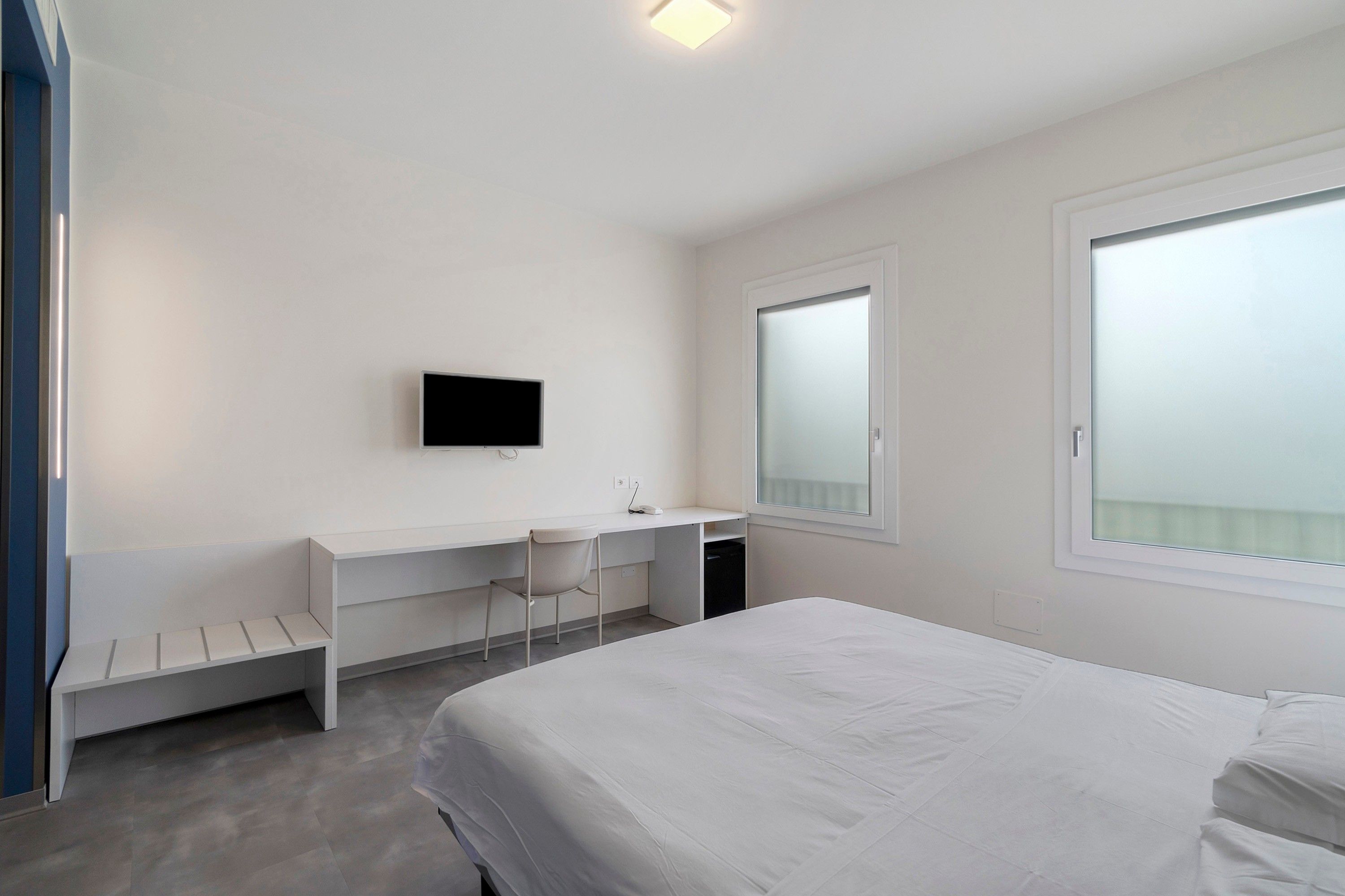 Une chambre d’hôtel moderne équipée d’un lit, d’un bureau, d’une chaise, d’une télévision et d’une fenêtre.
