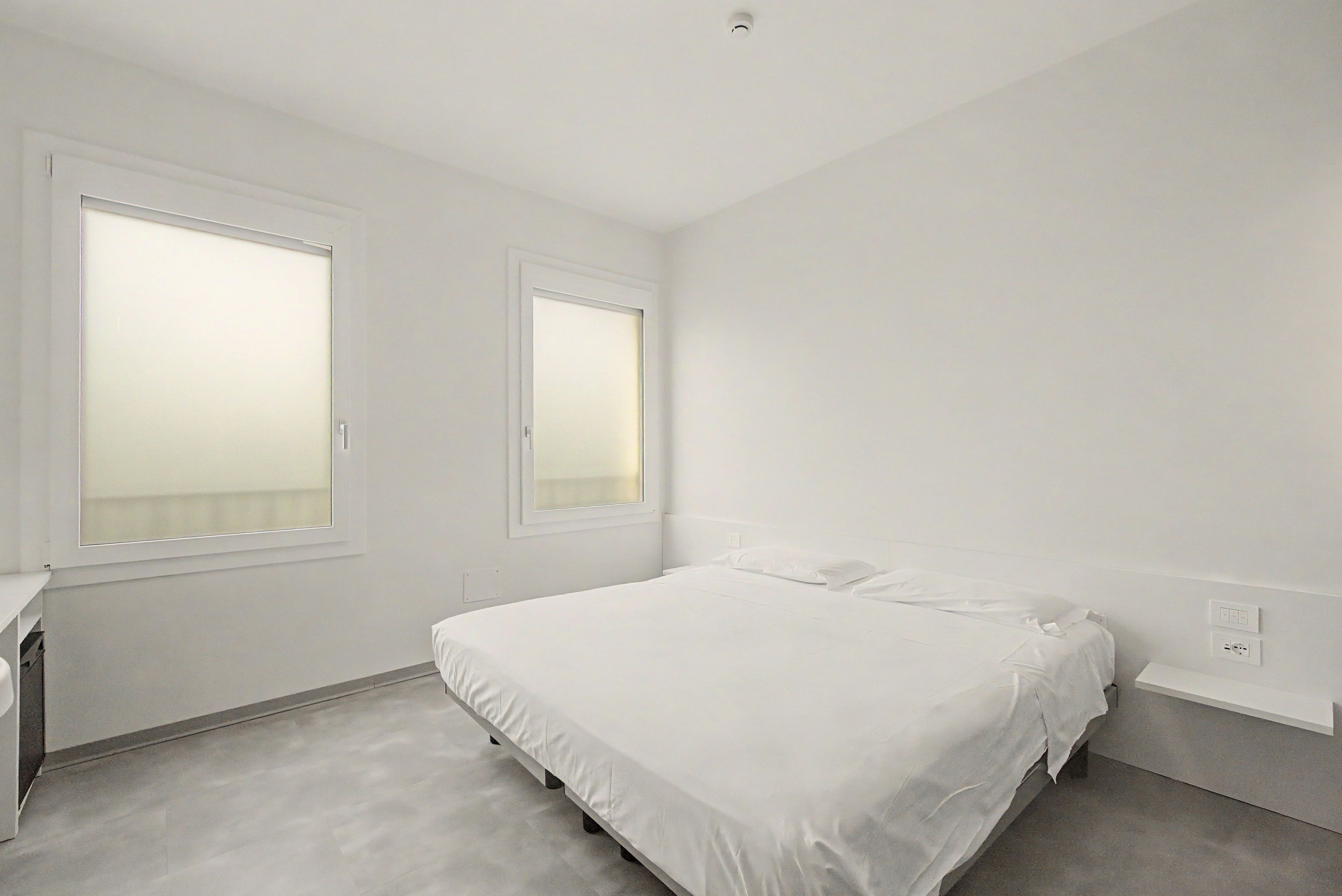 Une chambre à coucher avec un lit, deux fenêtres et un interrupteur sur le mur.