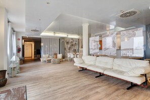 A spacious living area with a white sofa, wooden flooring, and a large window with artwork.