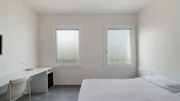 Een kleine, schone kamer met een bed, een bureau en twee ramen.