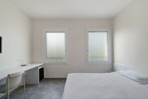 A small, clean room with a bed, a desk, and two windows.