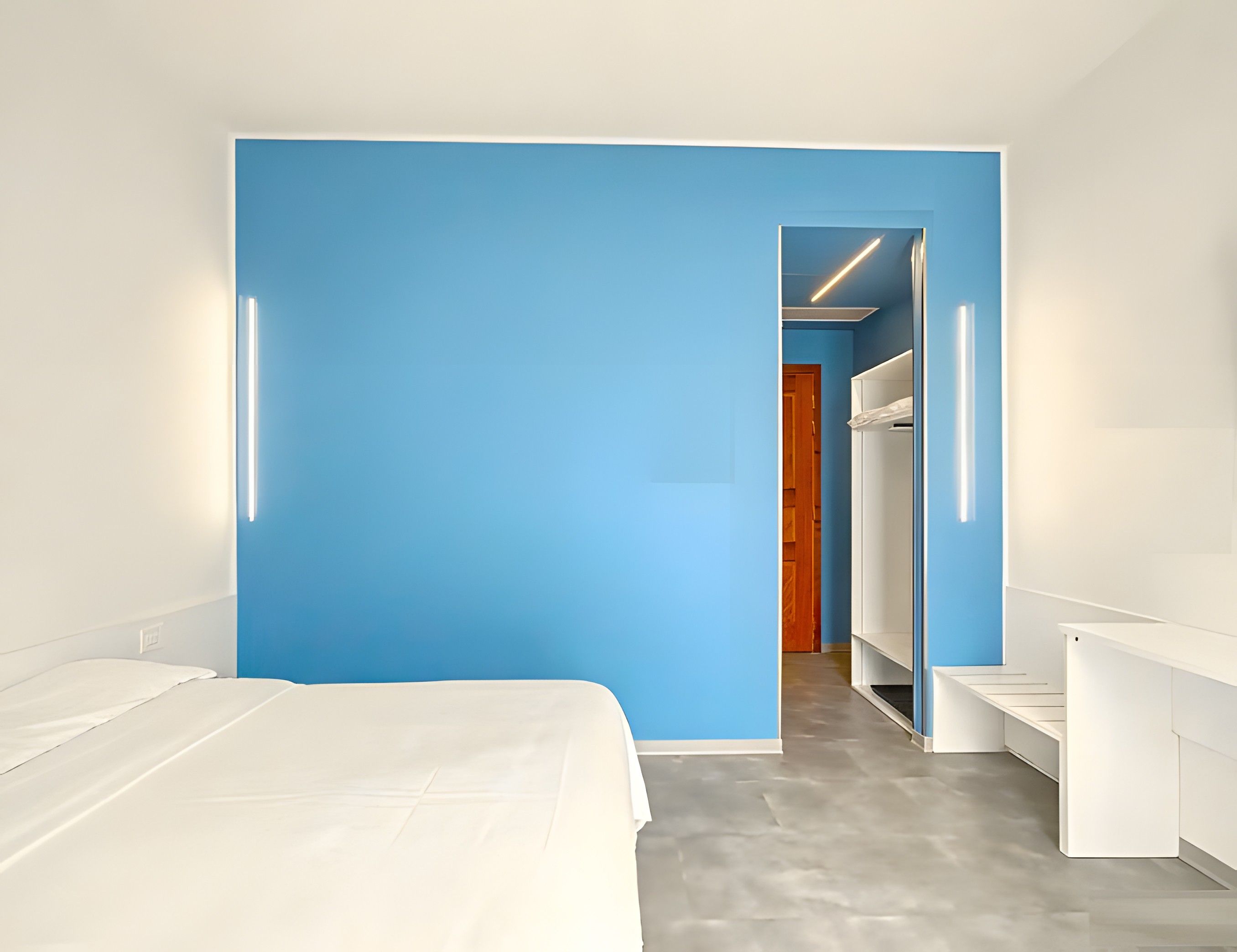 A modern hotel room with a large bed, a blue accent wall, and a walk-in closet.