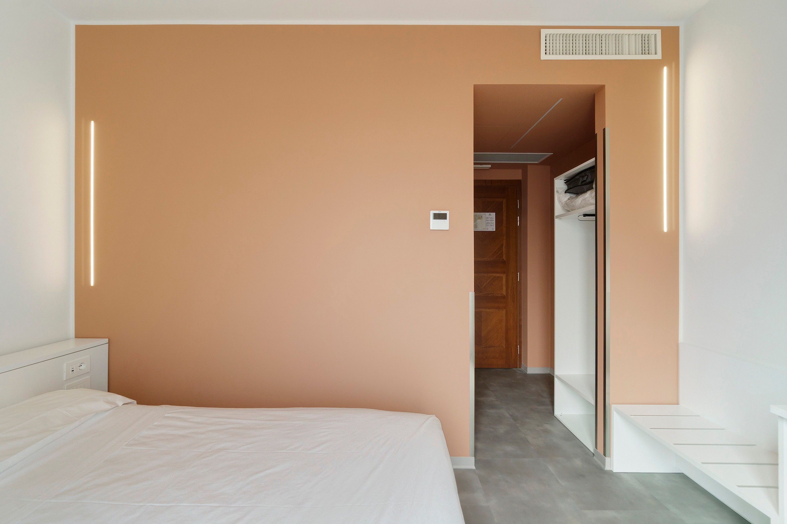 A hotel room with a bed, a wardrobe, and a door leading to a hallway.