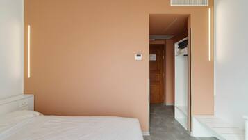 A hotel room with a bed, a wardrobe, and a door leading to a hallway.