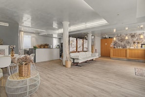 Una habitación amplia con piso de madera, un sofá blanco, un comedor con mesa y sillas, y una cocina con gabinetes de madera.