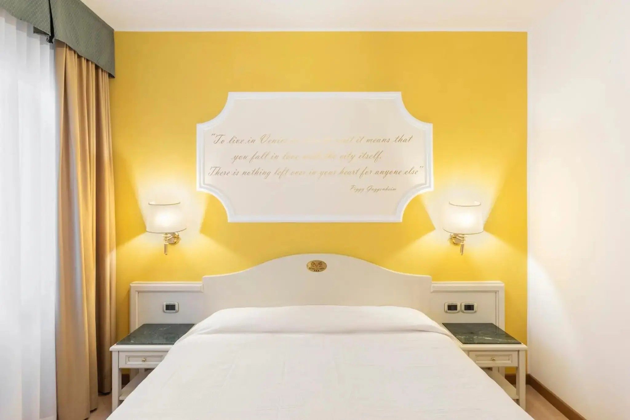 Una camera d'albergo con un letto, due comodini e una citazione appesa al muro.