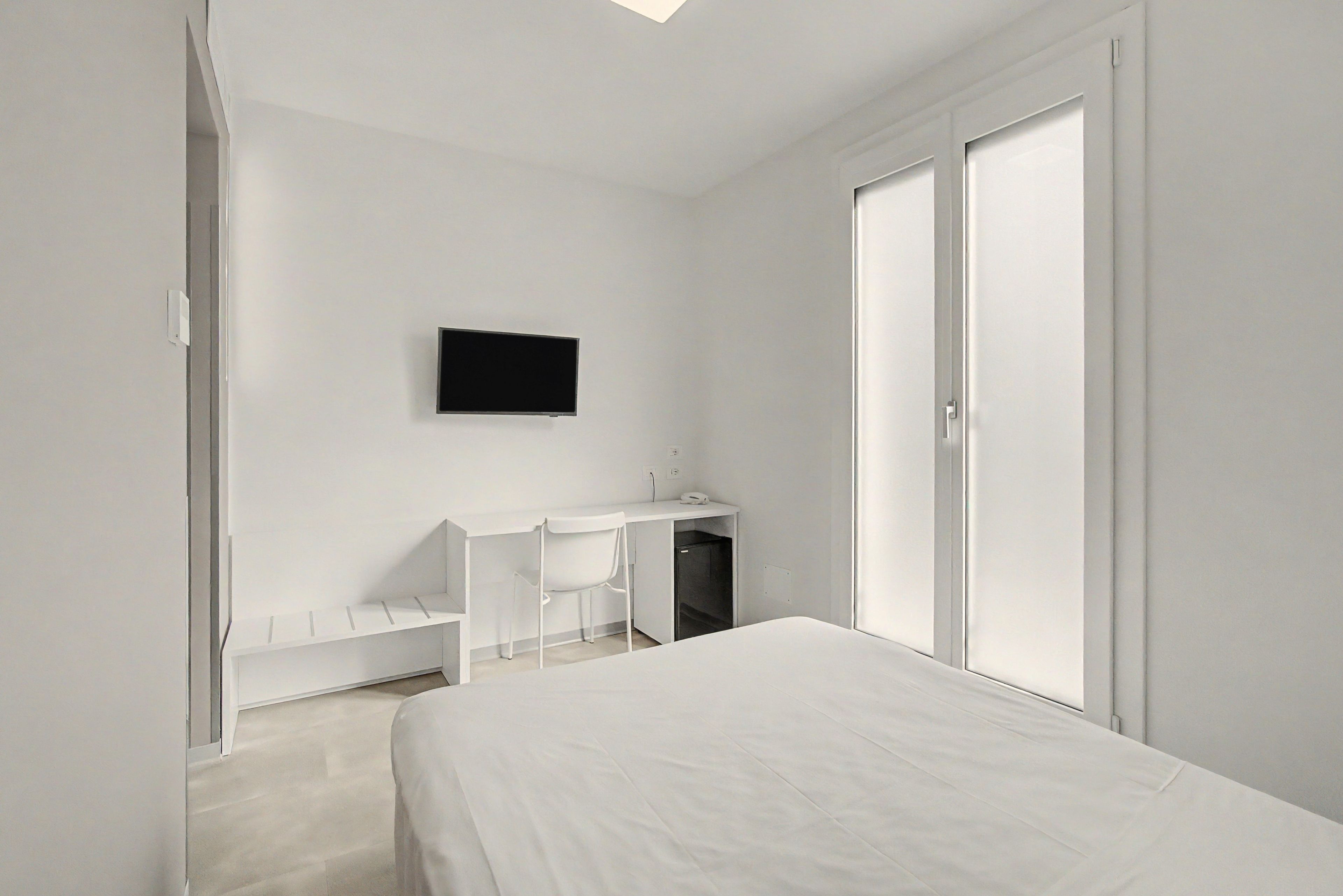 A minimalist bedroom with a bed, a desk, and a television on the wall.