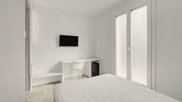 A minimalist bedroom with a bed, a desk, and a television on the wall.