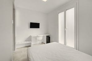 Un dormitorio minimalista con cama, escritorio y televisión en la pared.