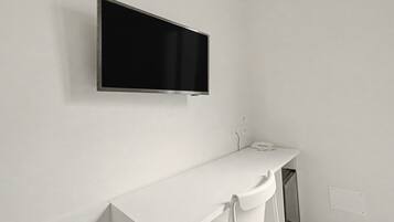 A white wall with a mounted television and a white counter with a telephone.