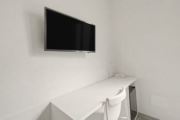 Pared blanca con un televisor montado y una encimera blanca con un teléfono.