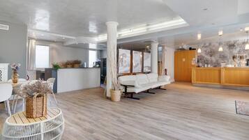 A spacious hotel lobby with a wooden floor, a white sofa, a reception desk, and a large window.