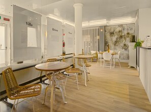 A modern interior with round tables and wicker chairs, white walls, and a wooden floor.
