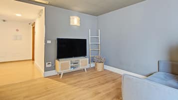 Een kamer met een flatscreen televisie op een houten standaard, een witte ladder en een rieten mand met gedroogde bloemen.