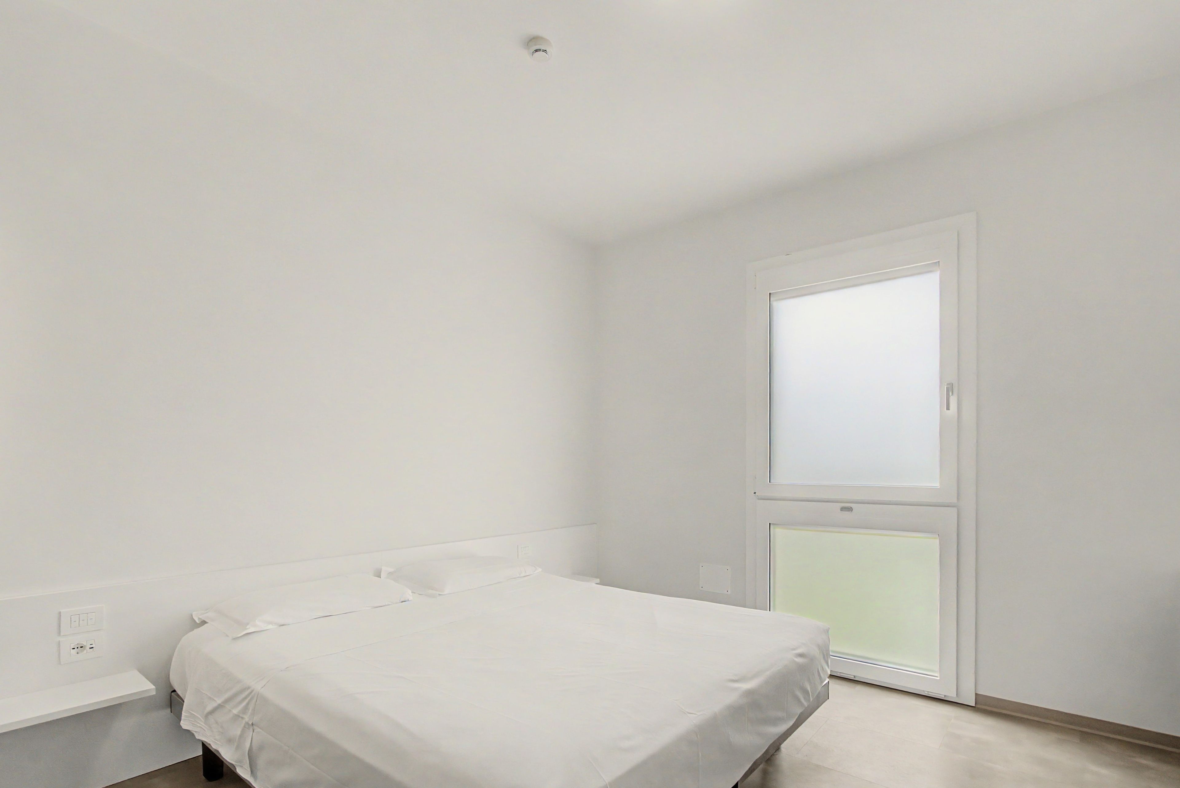 A minimalist bedroom with a single bed, a door with frosted glass panels, and a white ceiling.