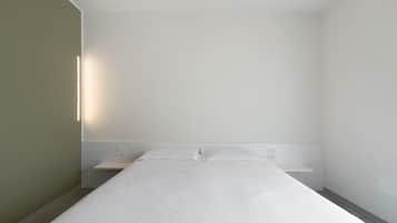 A minimalist hotel room with a single bed, bedside tables, and a wall-mounted light fixture.