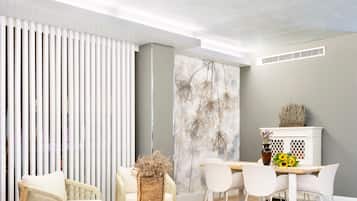 A modern living room with a dining area, featuring a white sofa, wicker furniture, and a decorative wall with a floral mural.