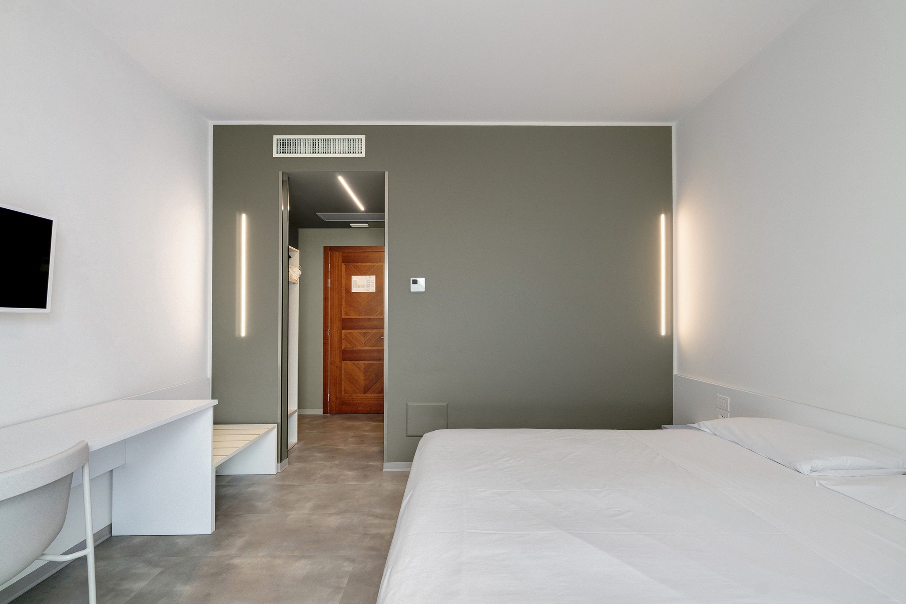 Ein modernes Hotelzimmer mit einem Bett, einem Schreibtisch und einem an der Wand befestigten Fernseher.