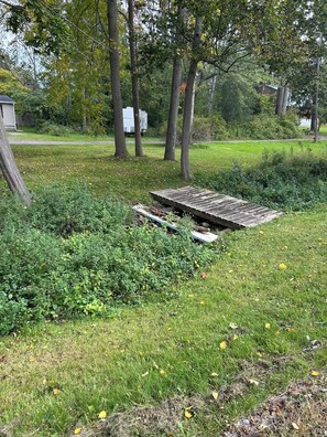 A grassy area with a wooden structure, surrounded by trees and a white trailer in the background. - Cozy 1-bedroom near letchworth on silver lake community (Castile)