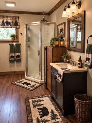 A bathroom with a glass shower enclosure, wooden cabinets, a sink with a mirror, and a towel rack with bear-themed towels. - Cozy 1-bedroom near letchworth on silver lake community (Castile)