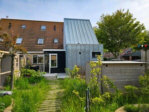 Ein modernes Haus mit Satteldach, einem kleinen Anbau und einem Garten mit einem Weg.