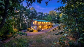 A two-story wooden cabin with a porch, surrounded by dense forest. - Secluded Yard • Pet-Friendly • Hot Tub (Sevierville)